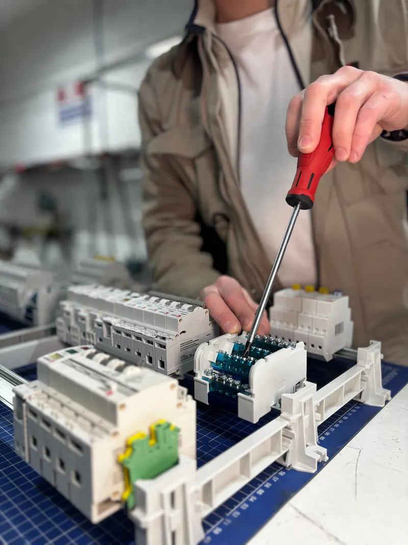 Hands using a screwdriver to assemble electrical components on a workbench