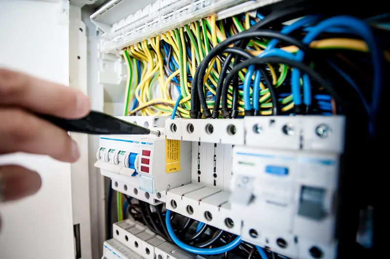 Close-up of wiring and an electrical panel, with a hand holding a tool