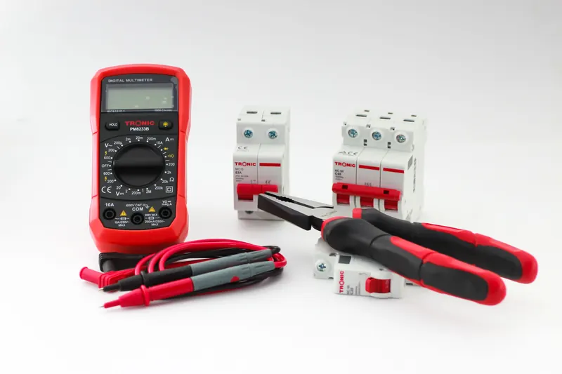 Digital multimeter, circuit breakers and pliers on a work surface