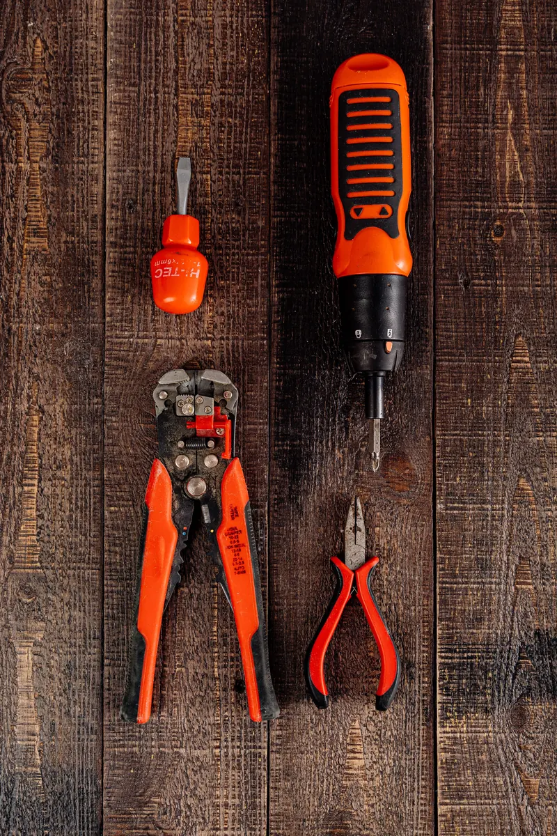 Electrical screwdriver, wire stripper and pliers on a wooden surface