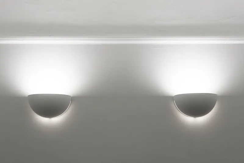 Two wall lights casting light upwards beneath white ceiling cornice